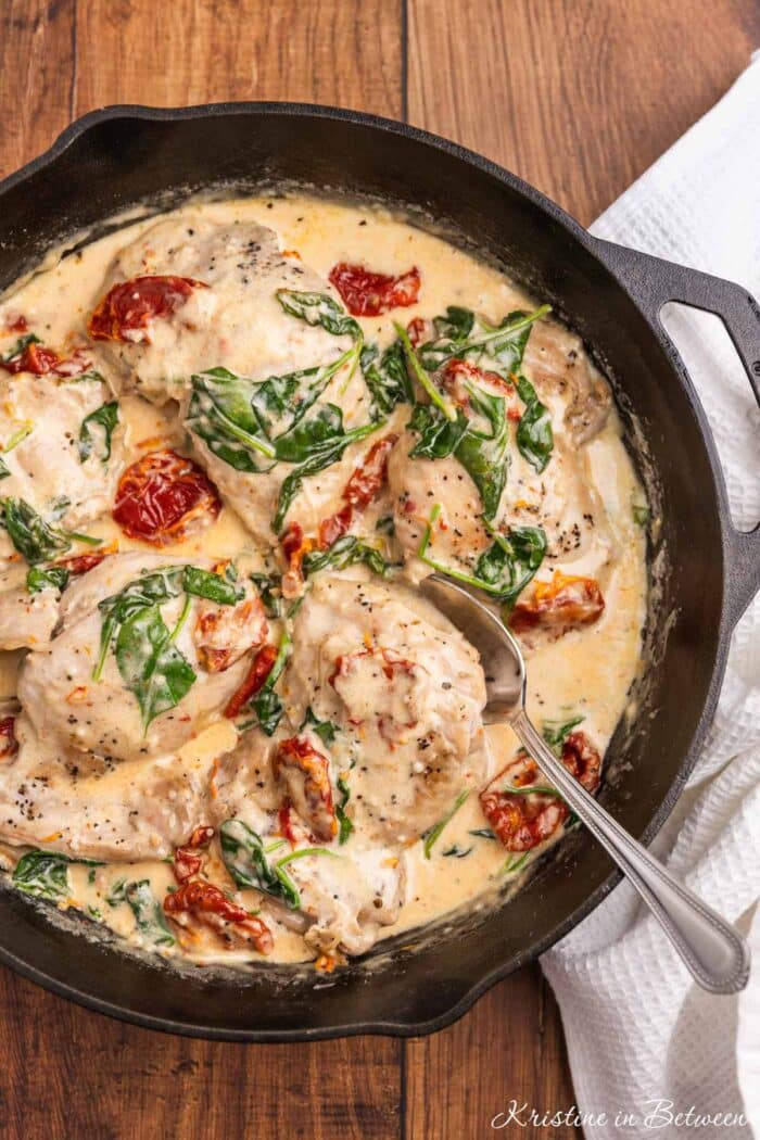 Creamy Tuscan chicken thighs with sun dried tomatoes and spinach in a cast iron pan with a spoon.