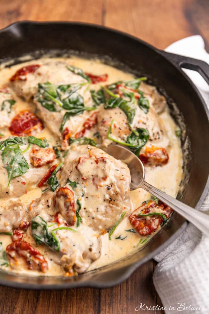 Creamy Tuscan chicken thighs with spinach and sun dried tomatoes in a cast iron pan.