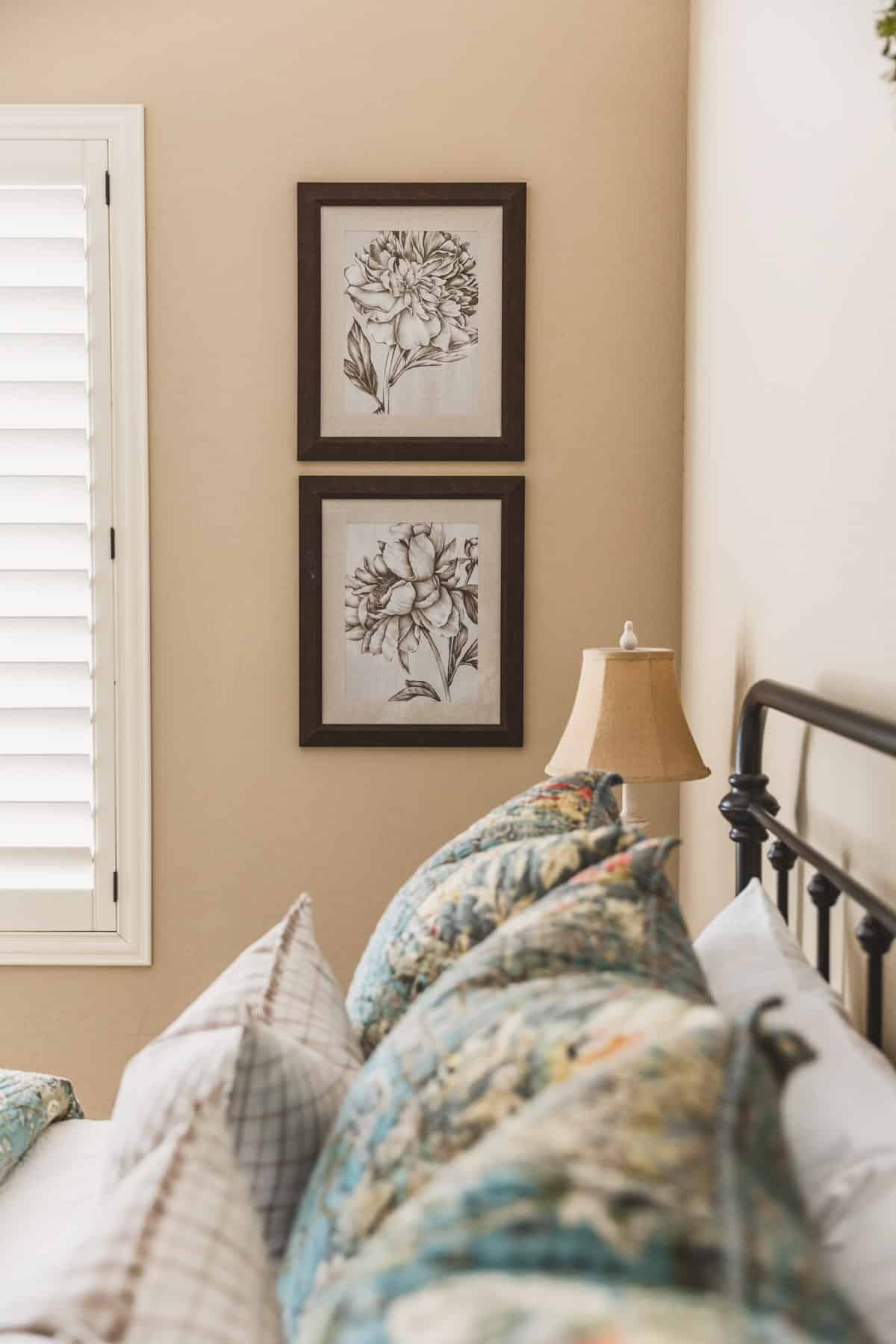A guest bedroom with blue quilted bedding, a metal bed, and some floral artwork on the wall.