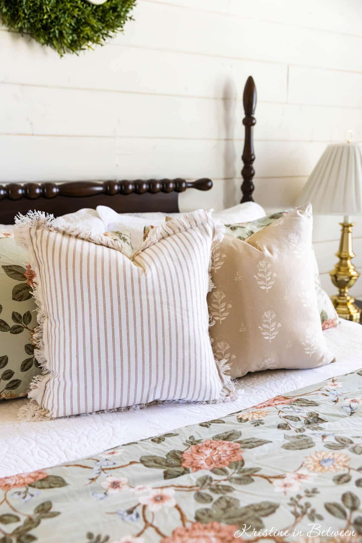 Miss matched throw pillows on a spindle bed with green floral duvet.