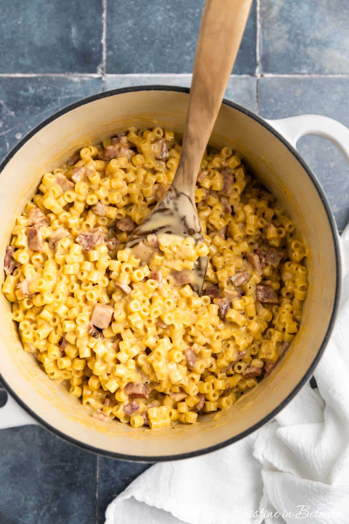 Macaroni and cheese with ham in a Dutch oven with a wooden spoon.