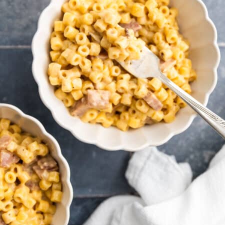 Macaroni and cheese with ham in a Dutch oven with a wooden spoon.