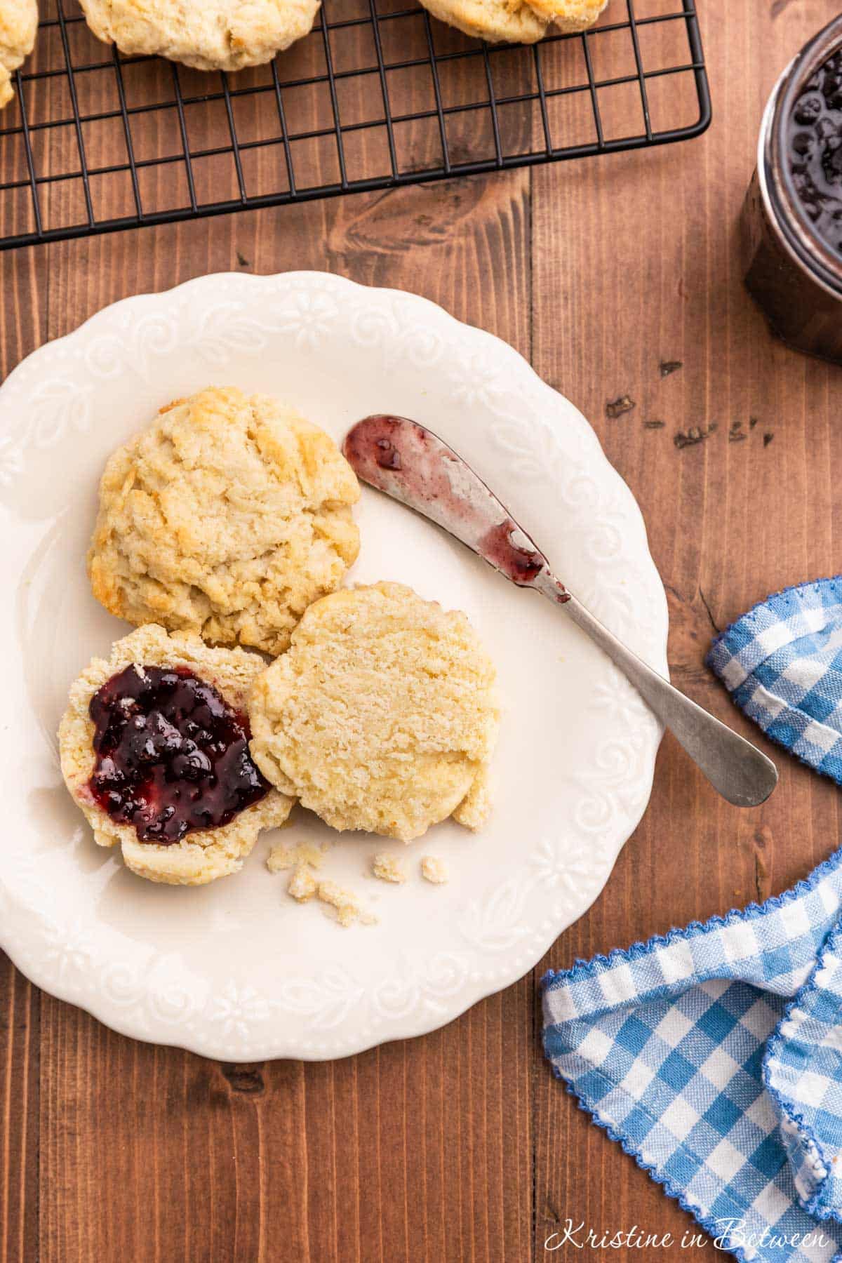 A plate of homemade biscuits cut in half with jam on it and a little spreader sitting next to them.