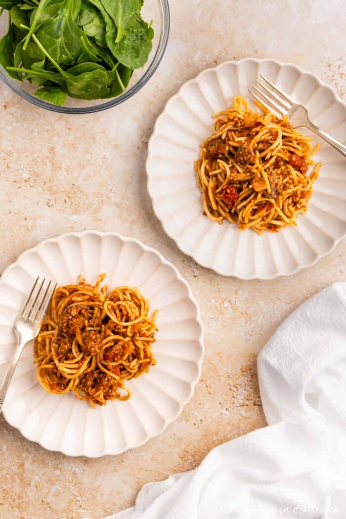 Two plates of spaghetti with meat sauce sitting next to a bowl of salad.