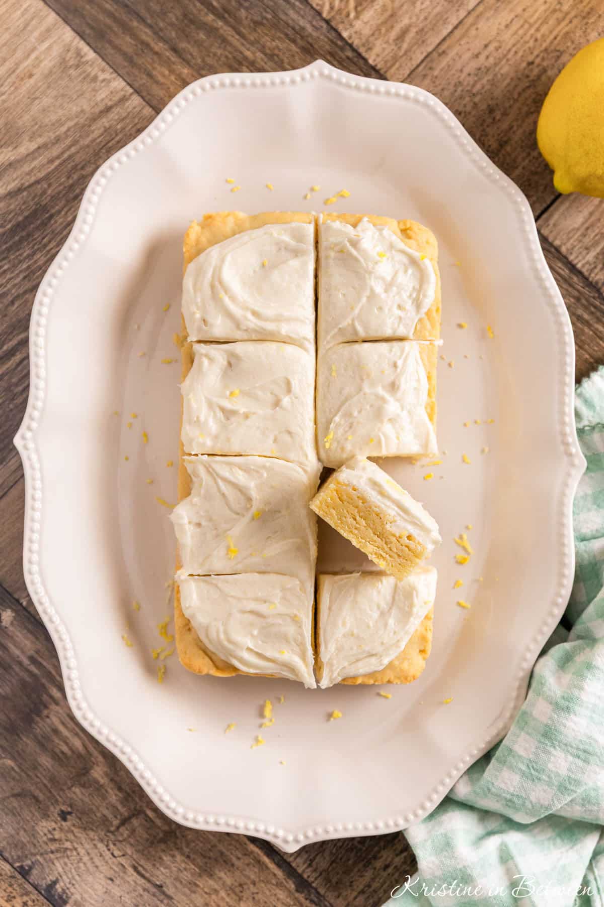 Lemon sugar cookie bars sitting on a white scalloped platter with a teal napkin next to them.