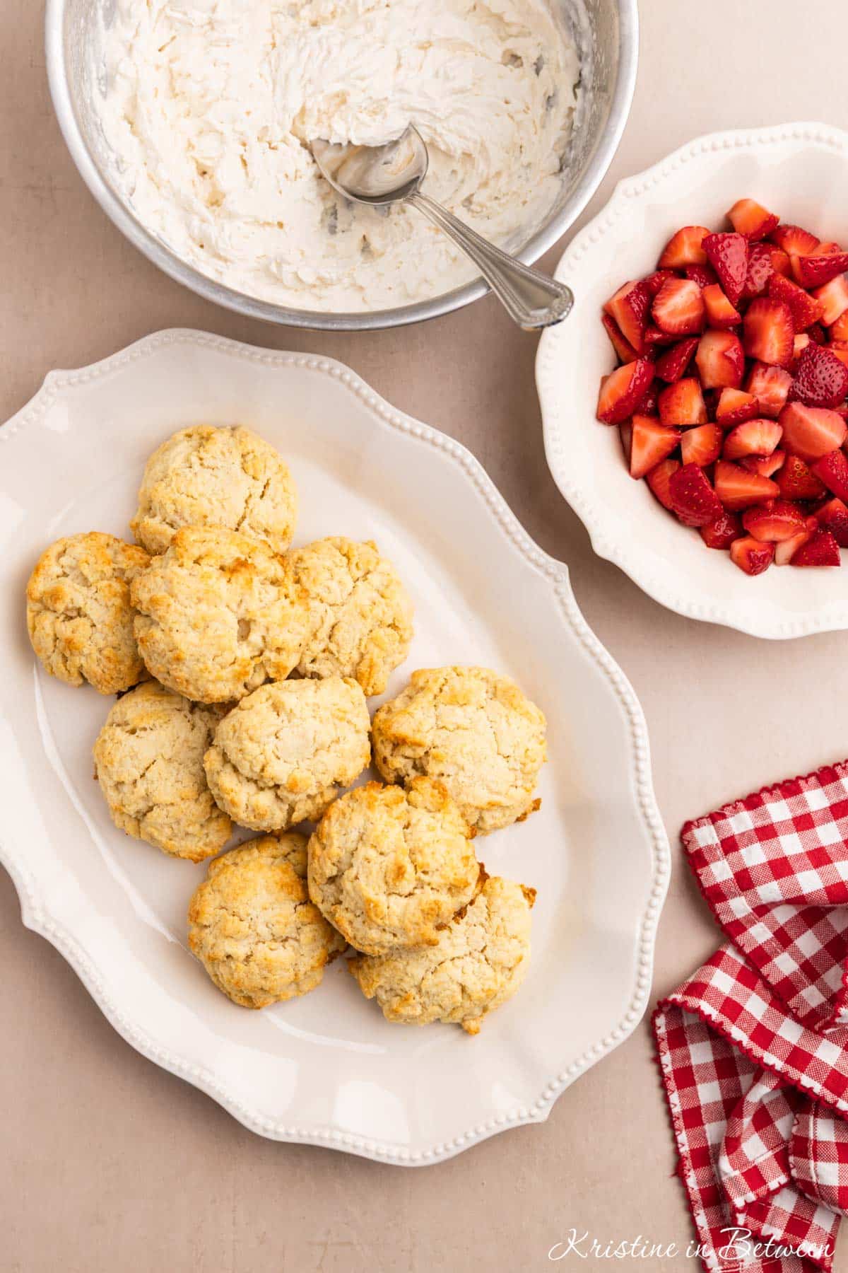 Homemade biscuits on a platter with strawberries and whipped cream sitting next to it.