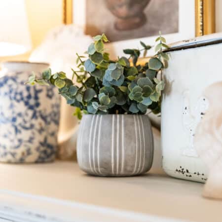 Cottage decor sitting on top of a white china cabinet with a small lamp.