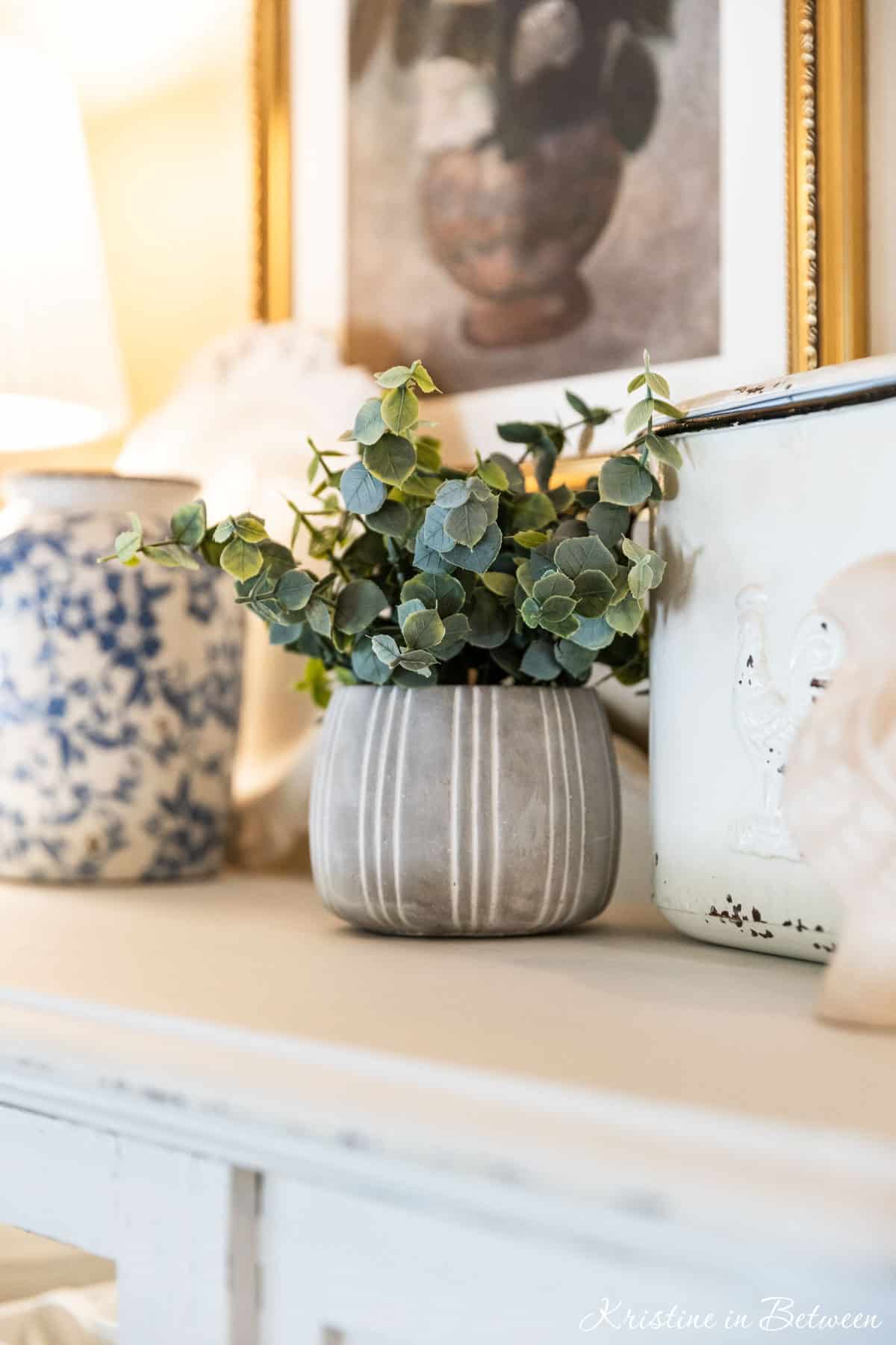 Cottage decor sitting on top of a white china cabinet with a small lamp.
