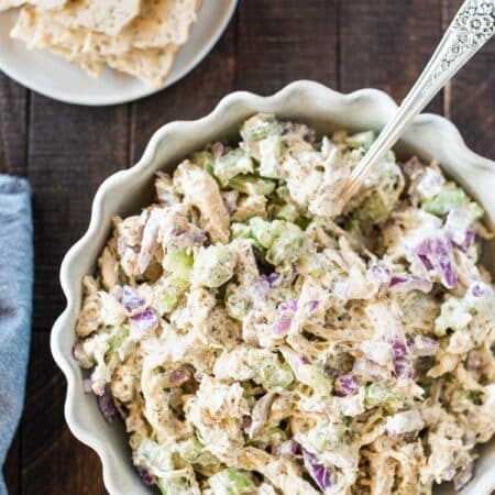 A bowl of prepared Greek yogurt chicken salad with a spoon in it and some crackers on the side.