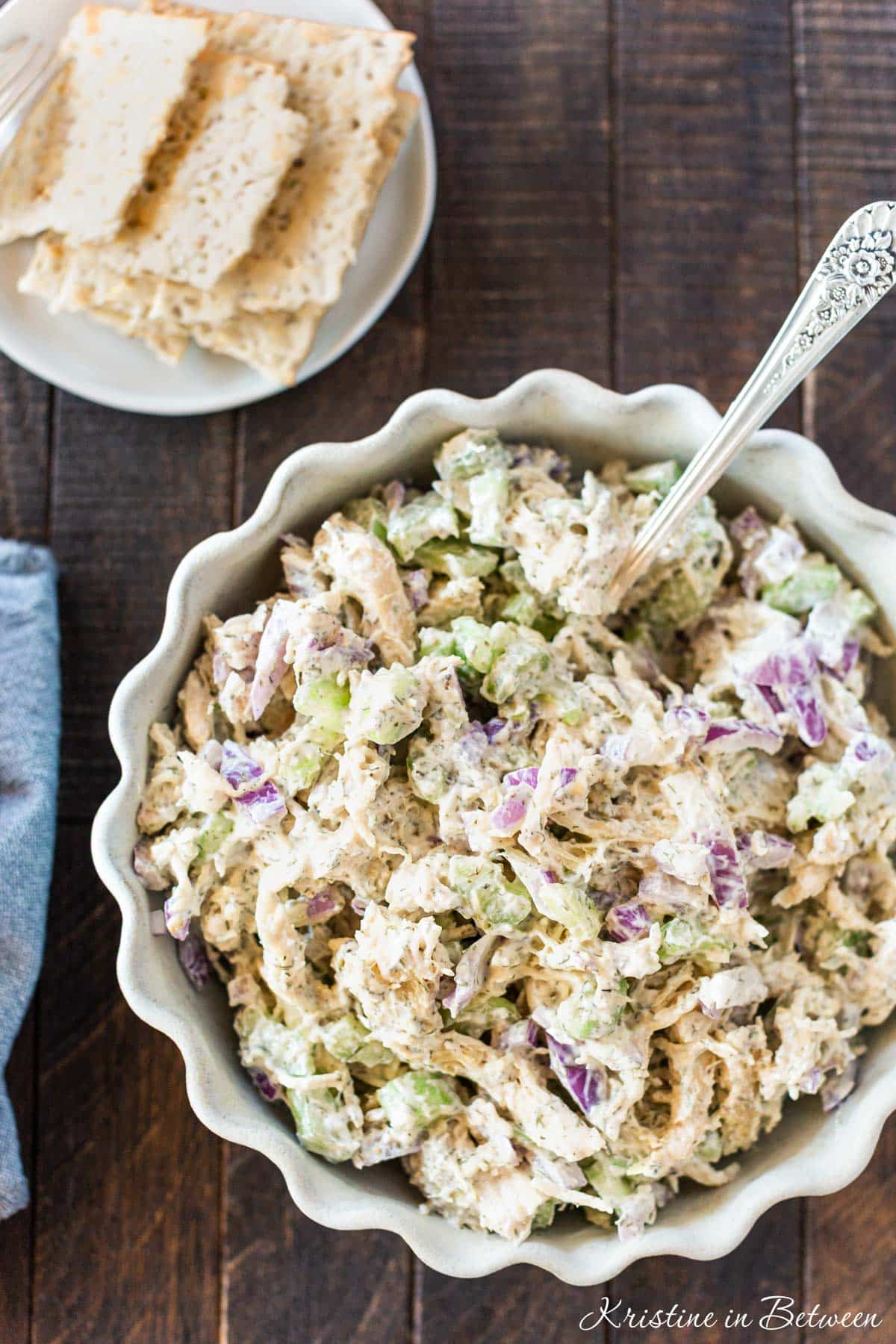 A bowl of prepared Greek yogurt chicken salad with a spoon in it and some crackers on the side.