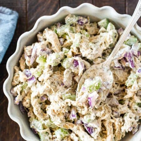 Chicken salad in a white scalloped bowl with a spoon on top and a bite on the spoon.