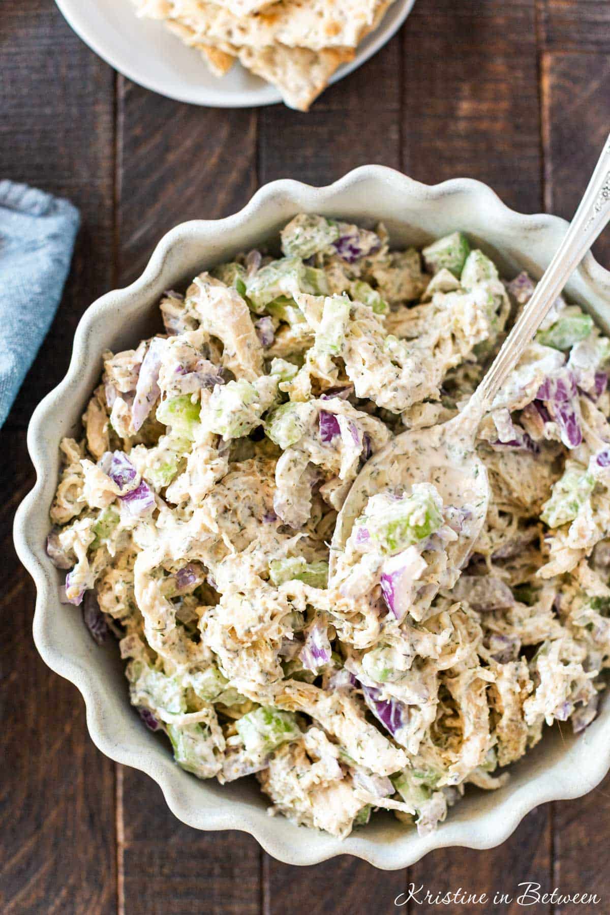 Chicken salad in a white scalloped bowl with a spoon on top and a bite on the spoon.