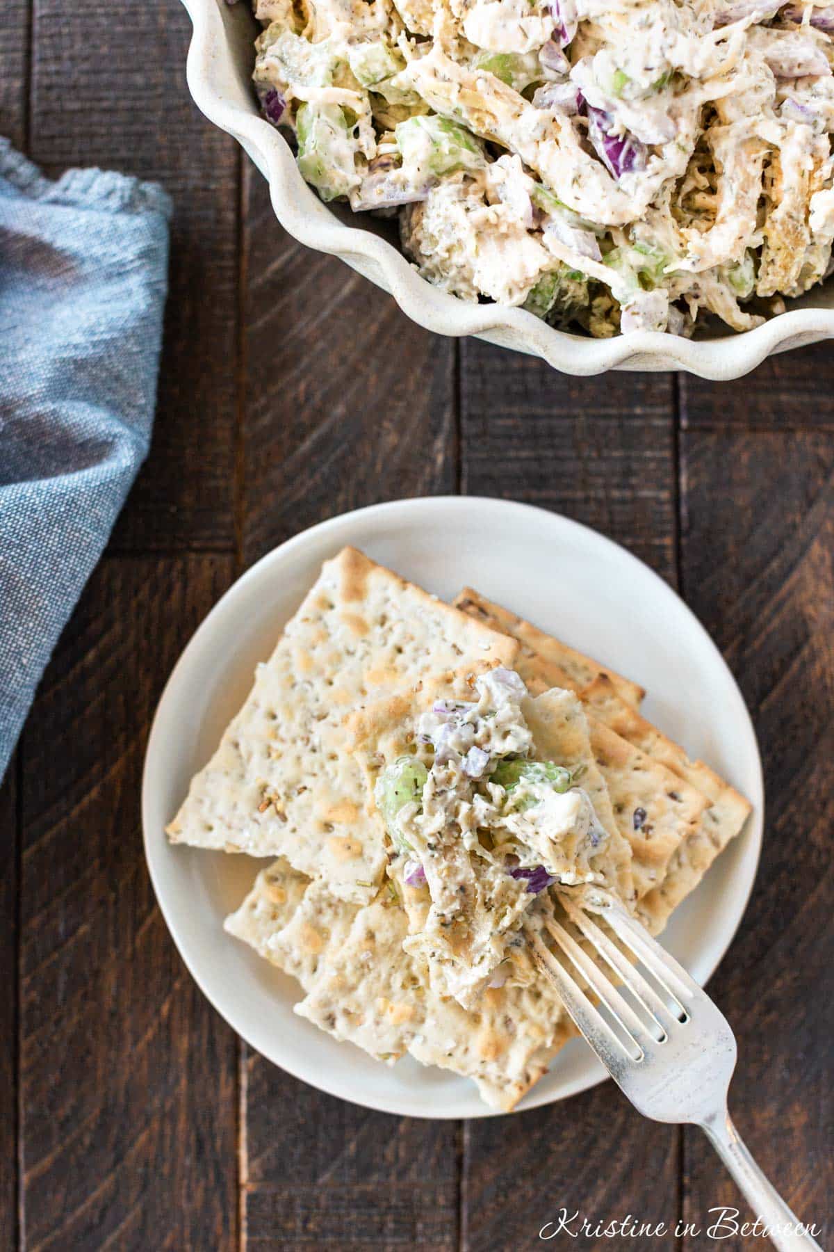 Crackers on a white plate with a bite of chicken salad on top and a fork laying next to them.