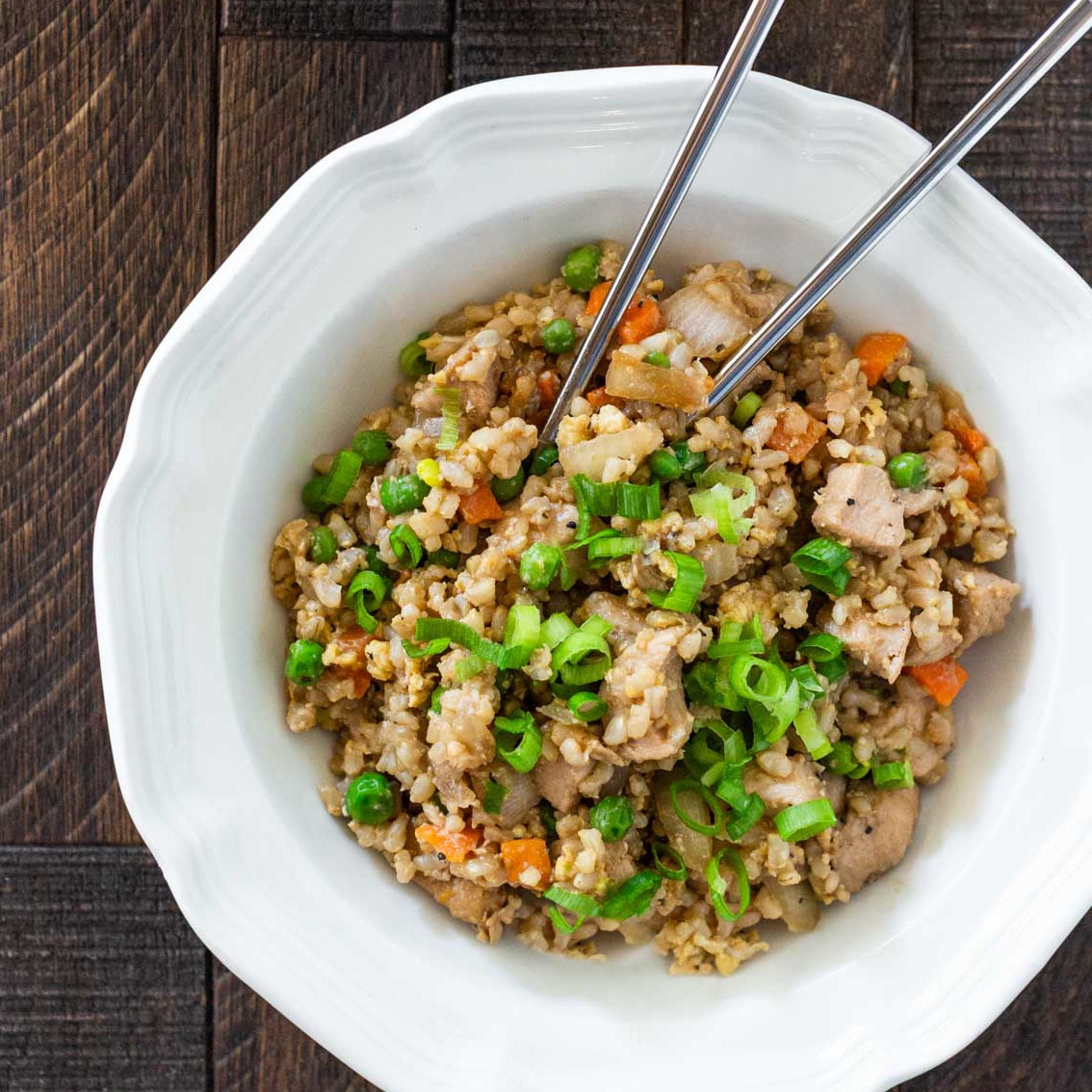 A bowl of chicken fried rice with sliced green onions sprinkled on top.