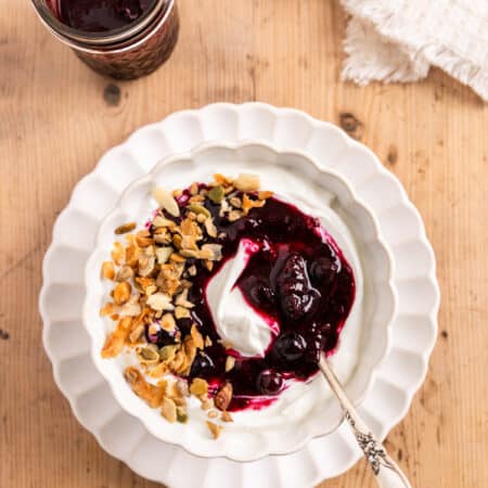 Blueberry chia jam over some yogurt in a white bowl with a spoon.