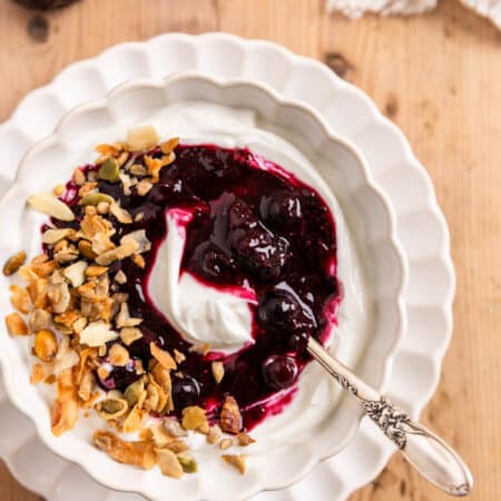 Blueberry chia jam over some yogurt in a white bowl with a spoon.