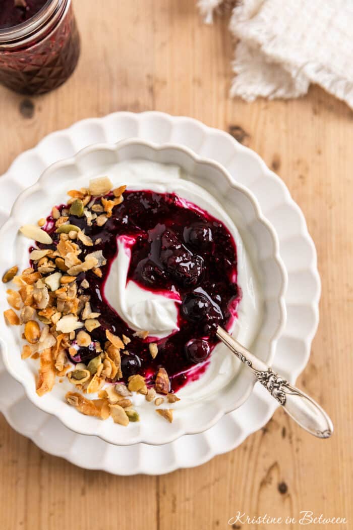 Blueberry chia jam over some yogurt in a white bowl with a spoon.