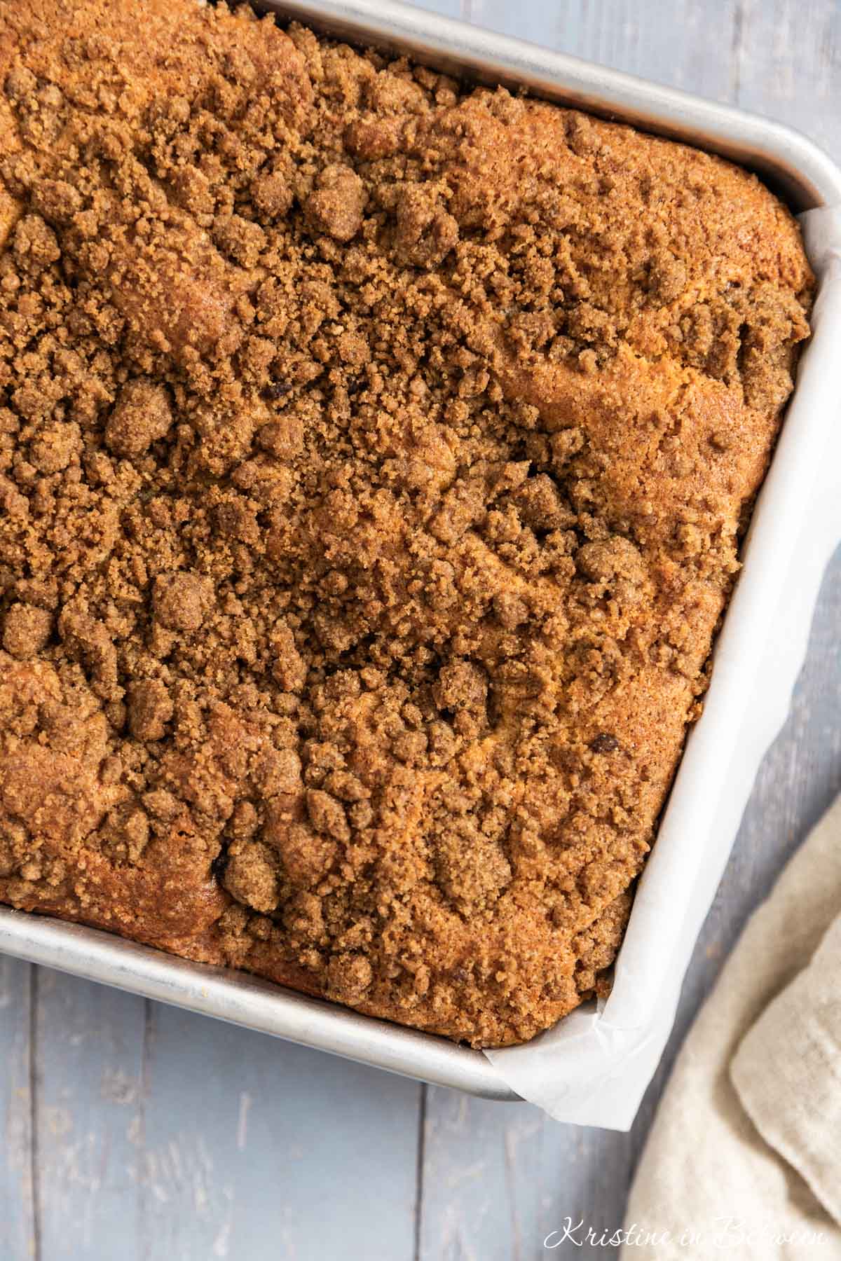 Cinnamon coffee cake in a metal baking pan with a napkin laying next to it.