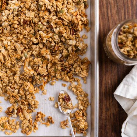 Homemade granola on an aluminum baking sheet with a spoon sitting next to it.