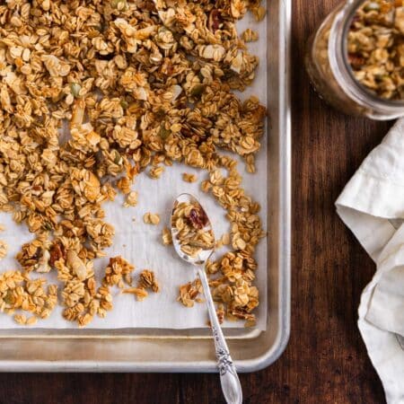 Homemade granola on an aluminum baking sheet with a spoon sitting next to it.