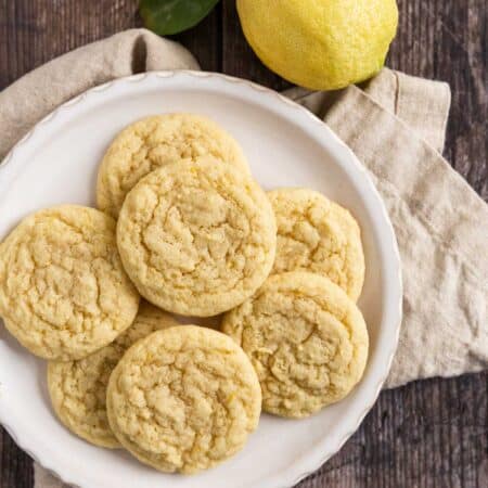 Lemon sugar cookies on a white plate with a beige napkin and a lemon off a tree sitting next to them.