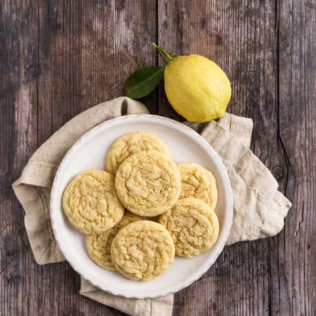 Lemon sugar cookies on a white plate with a beige napkin and a lemon off a tree sitting next to them.