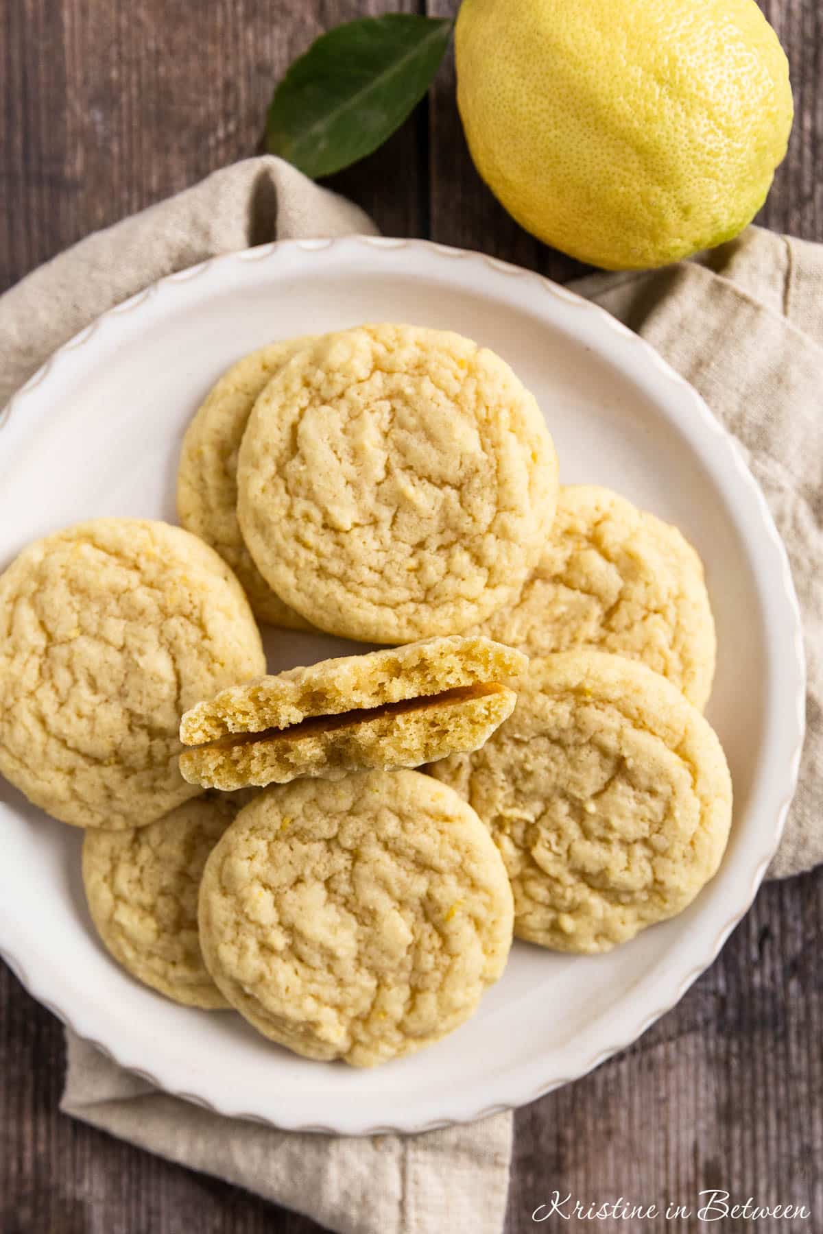 Lemon sugar cookies on a white plate with a beige napkin and a lemon off a tree sitting next to them.