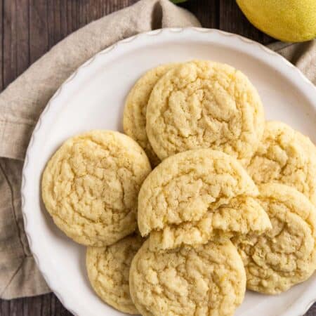 Lemon sugar cookies on a white plate with a beige napkin and a lemon off a tree sitting next to them.