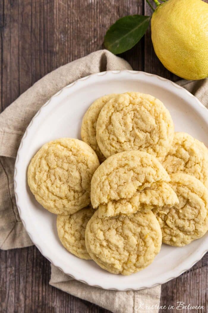 Lemon sugar cookies on a white plate with a beige napkin and a lemon off a tree sitting next to them.