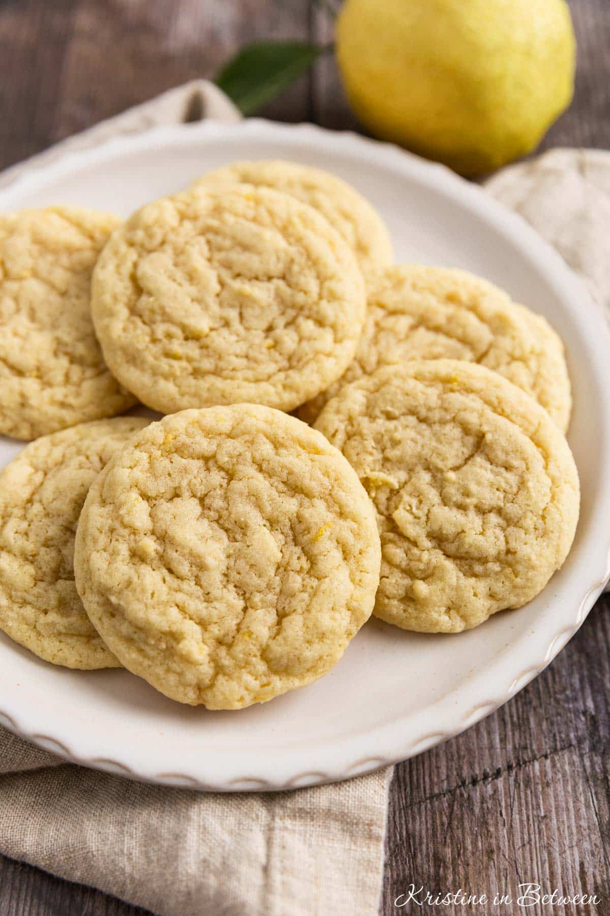 Lemon sugar cookies on a white plate with a beige napkin and a lemon off a tree sitting next to them.