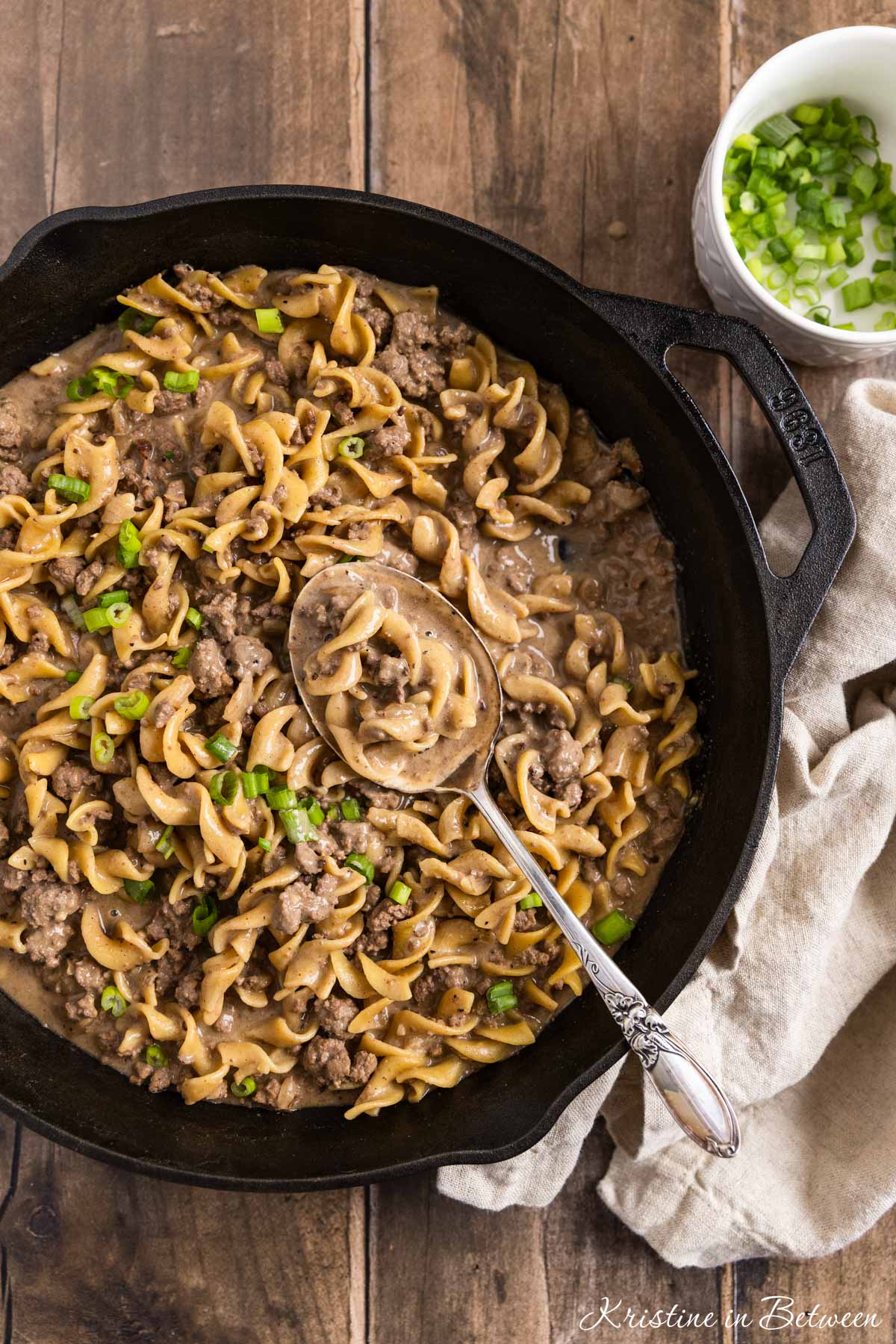 A cast iron skillet of ground beef stroganoff with a spoon in it, ready to eat.