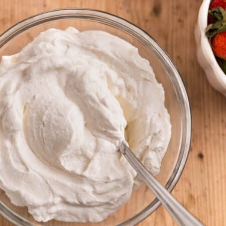 A bowl of homemade whipped cream in a glass bowl with a spoon sitting next to small bowls of berries.