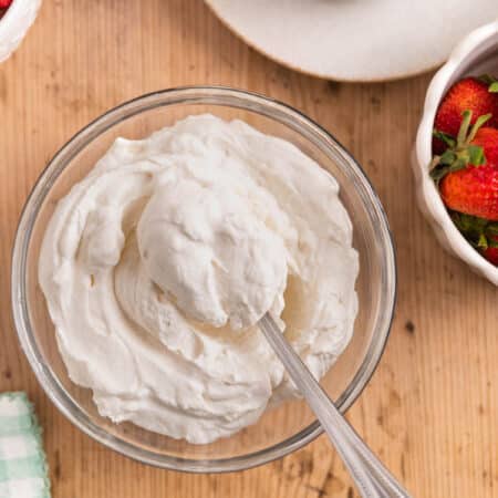 A bowl of homemade whipped cream in a glass bowl with a spoon sitting next to small bowls of berries.
