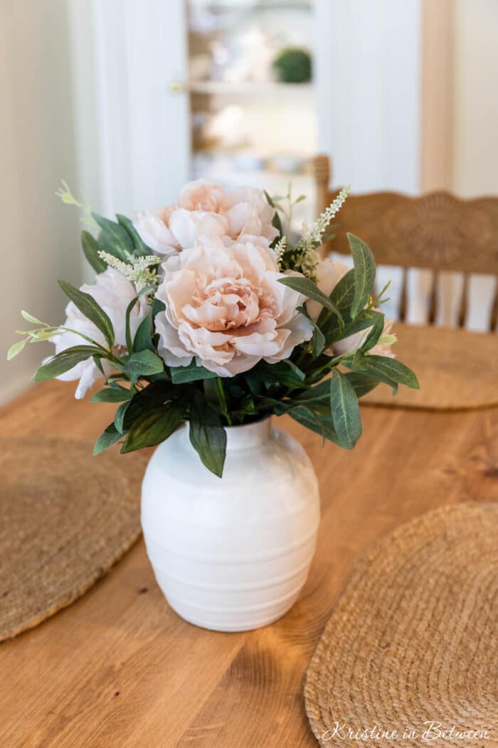 Artificial flowers in a vase on a wooden table.