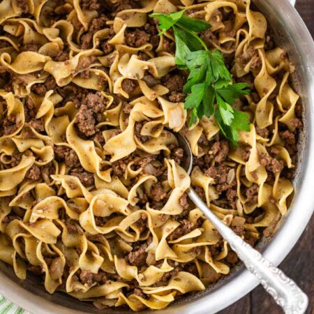 Cooked beef and noodles in a stainless steel pan with a spoon in it.