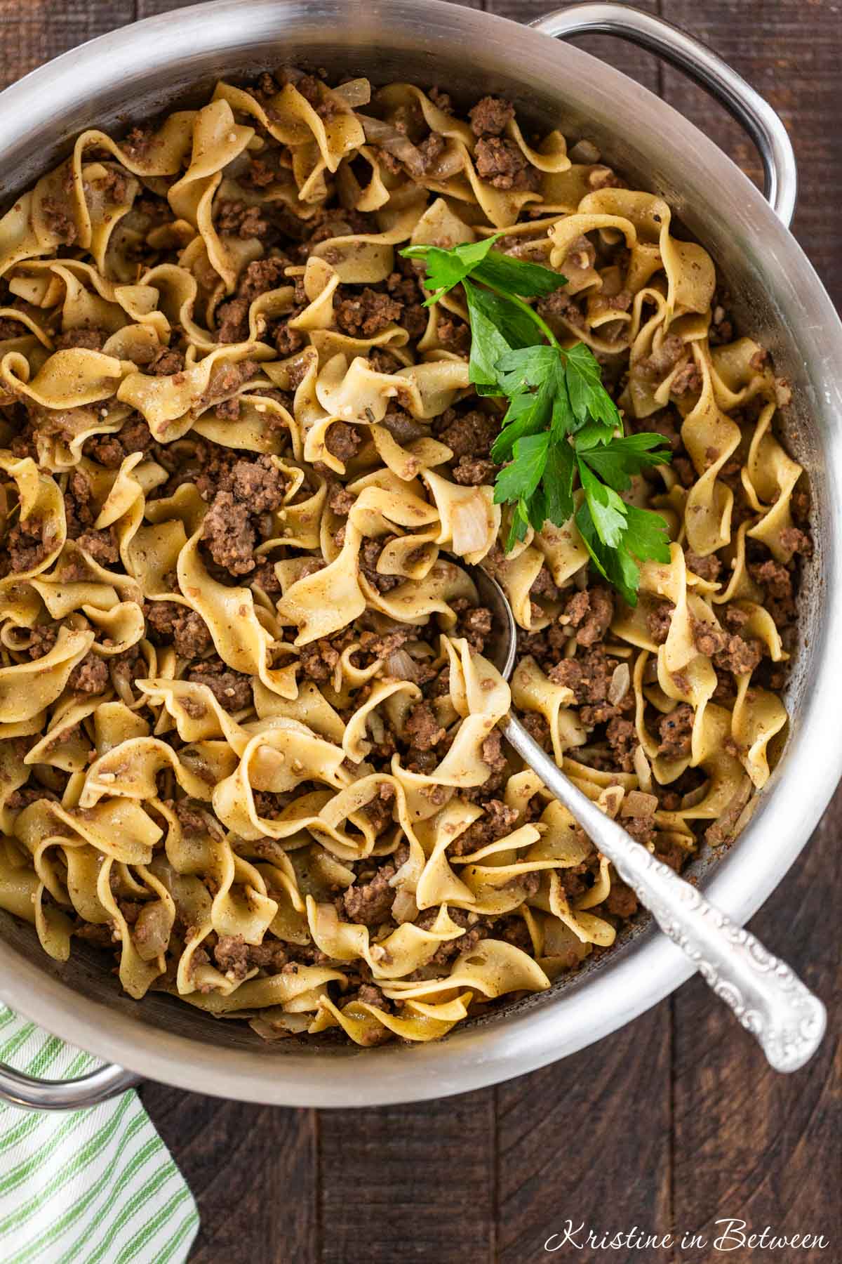 Cooked beef and noodles in a stainless steel pan with a spoon in it.