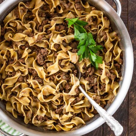 Cooked beef and noodles in a stainless steel pan with a spoon in it.