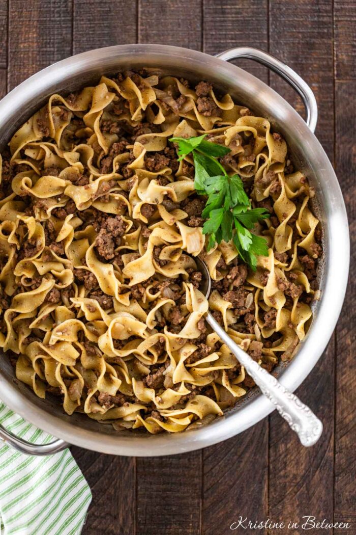 Cooked beef and noodles in a stainless steel pan with a spoon in it.