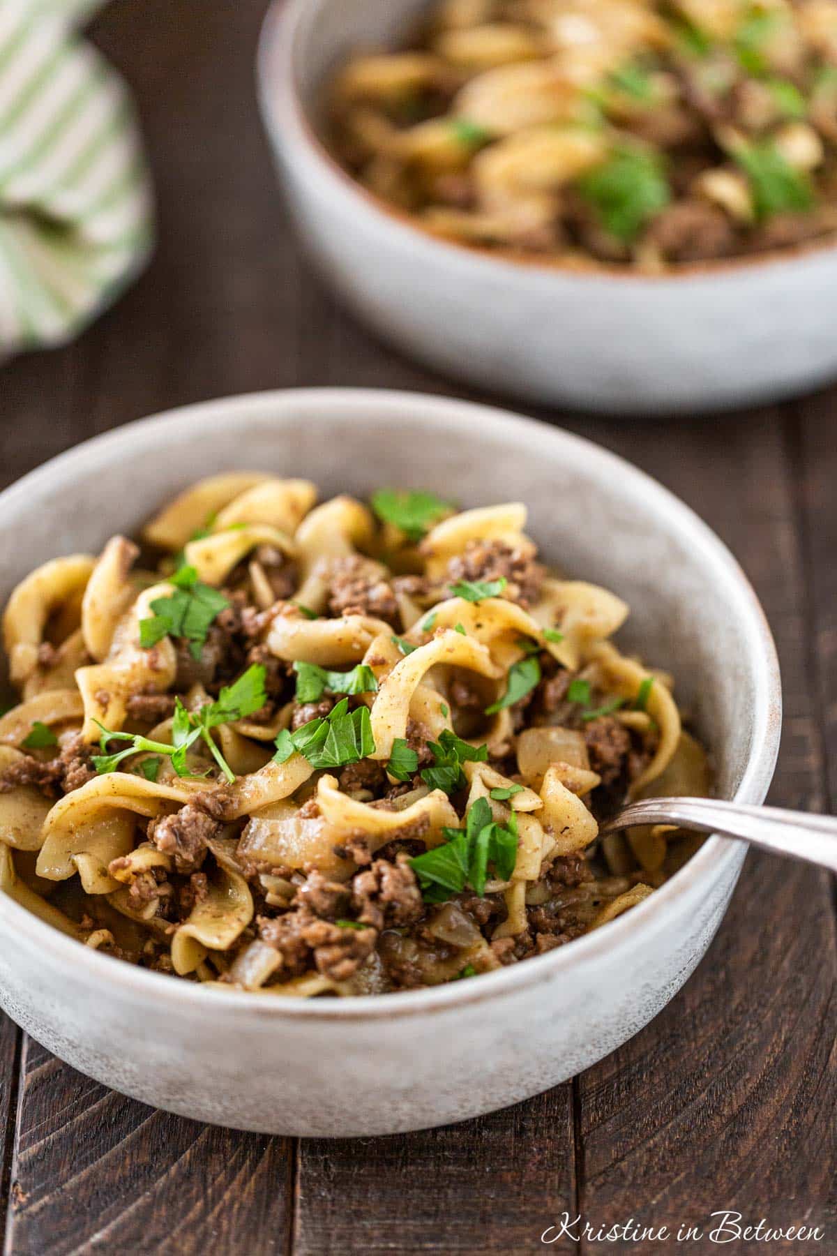 A bowl of cooked beef and noodles with a fork in it ready to eat.