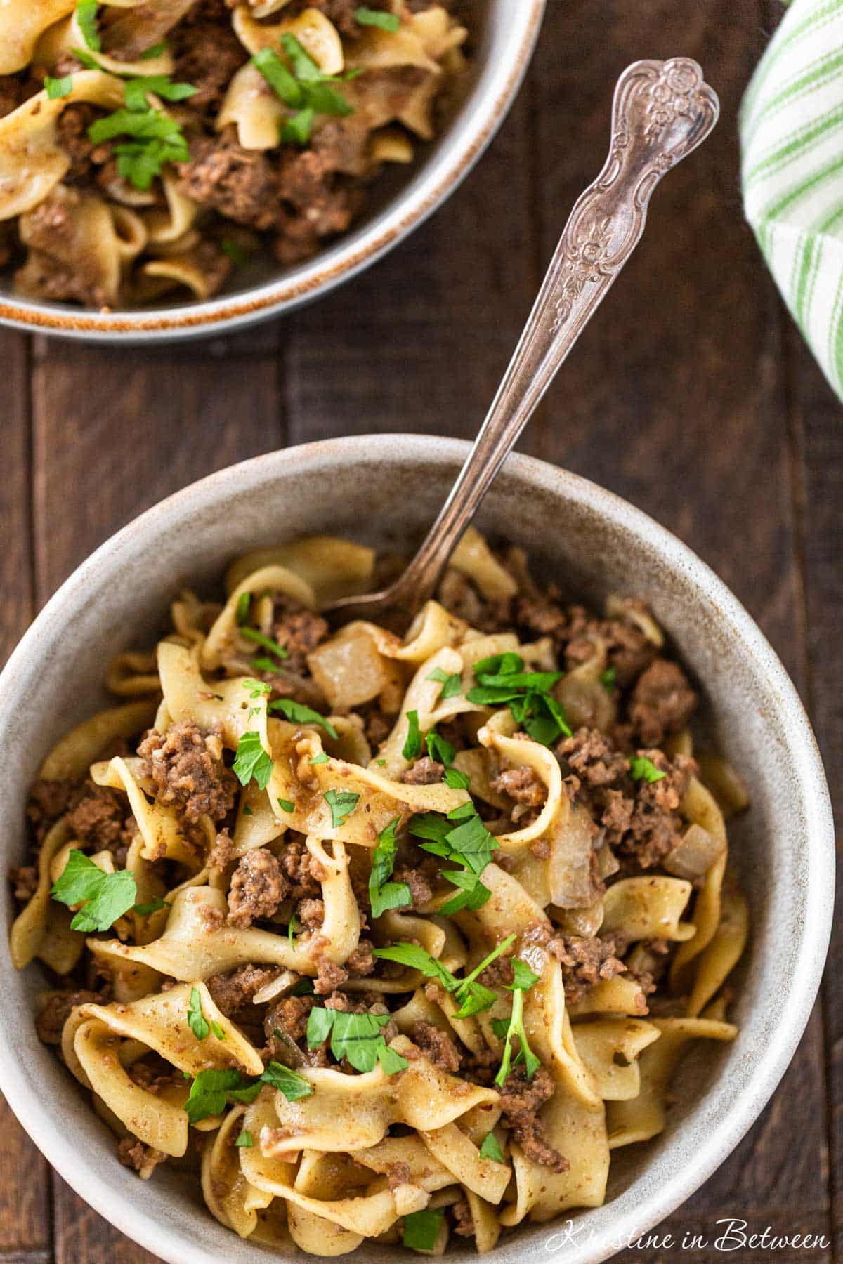 A bowl of cooked beef and noodles with a fork in it ready to eat.