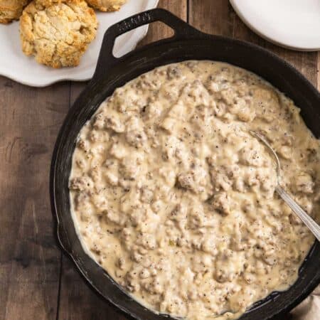 A pan of sausage gravy with a spoon in it and a plate of biscuits sitting next to it.