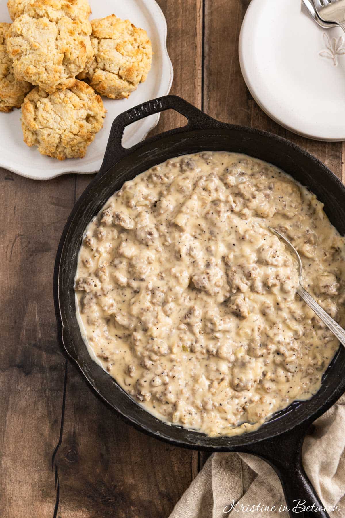 A pan of sausage gravy with a spoon in it and a plate of biscuits sitting next to it.