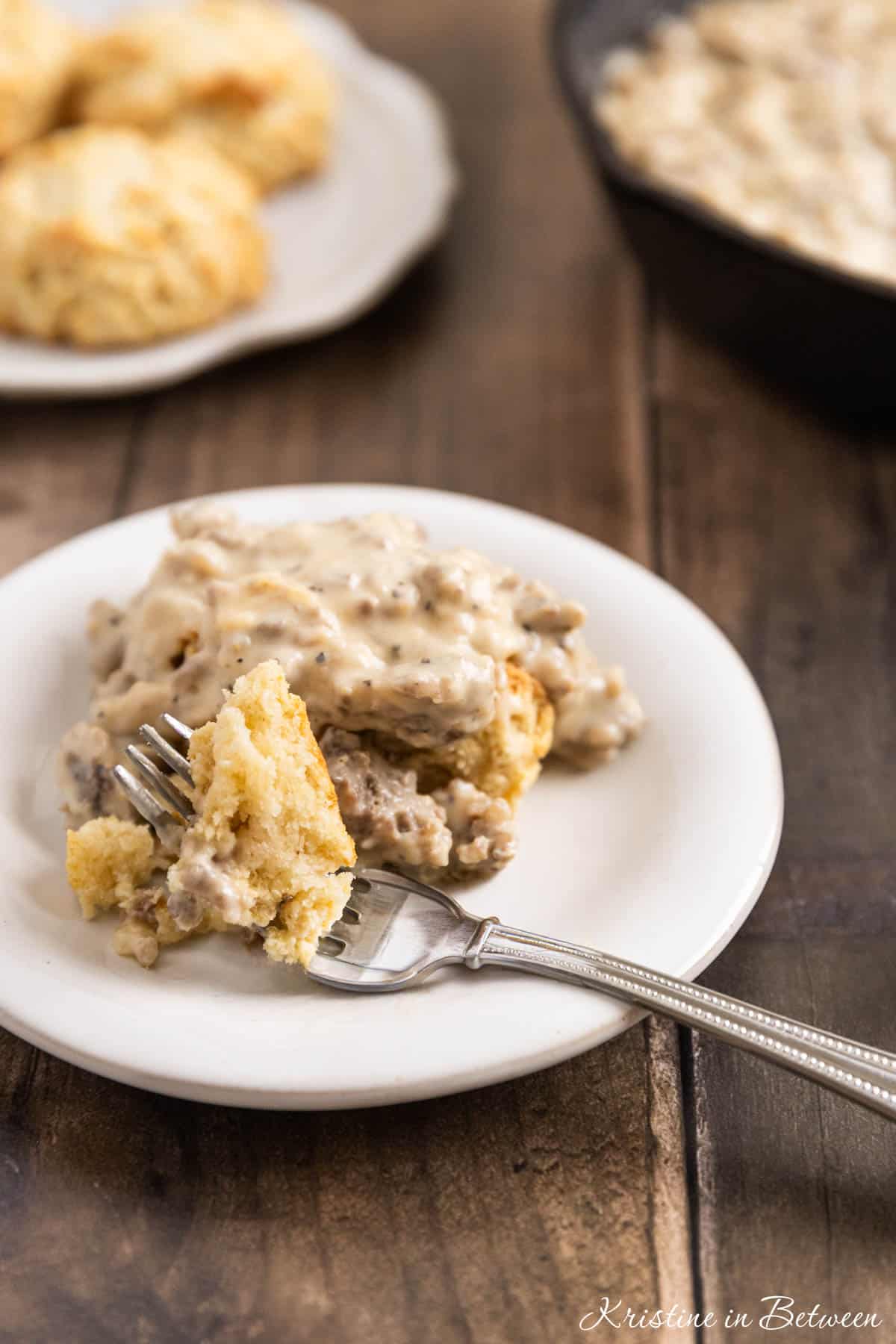 A small plate of biscuits and gravy with a fork sitting with it.