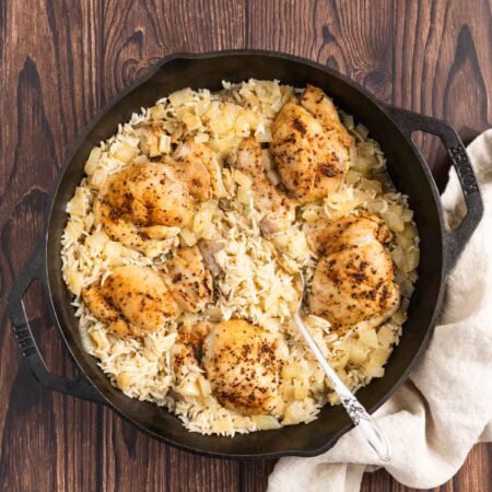 Chicken thighs and rice in a cast iron pan with an antique spoon.