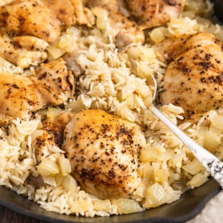 Chicken thighs and rice in a cast iron pan with an antique spoon.