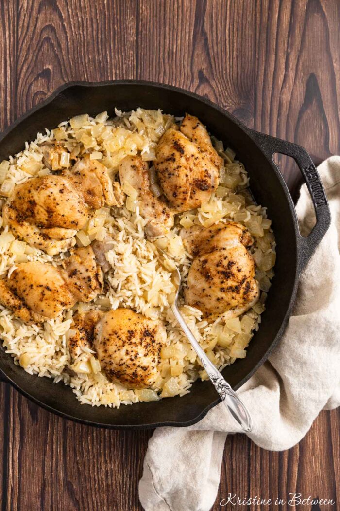 Chicken thighs and rice in a cast iron pan with an antique spoon.