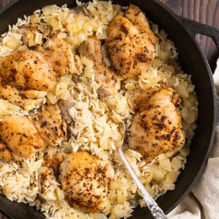 Chicken thighs and rice in a cast iron pan with an antique spoon.