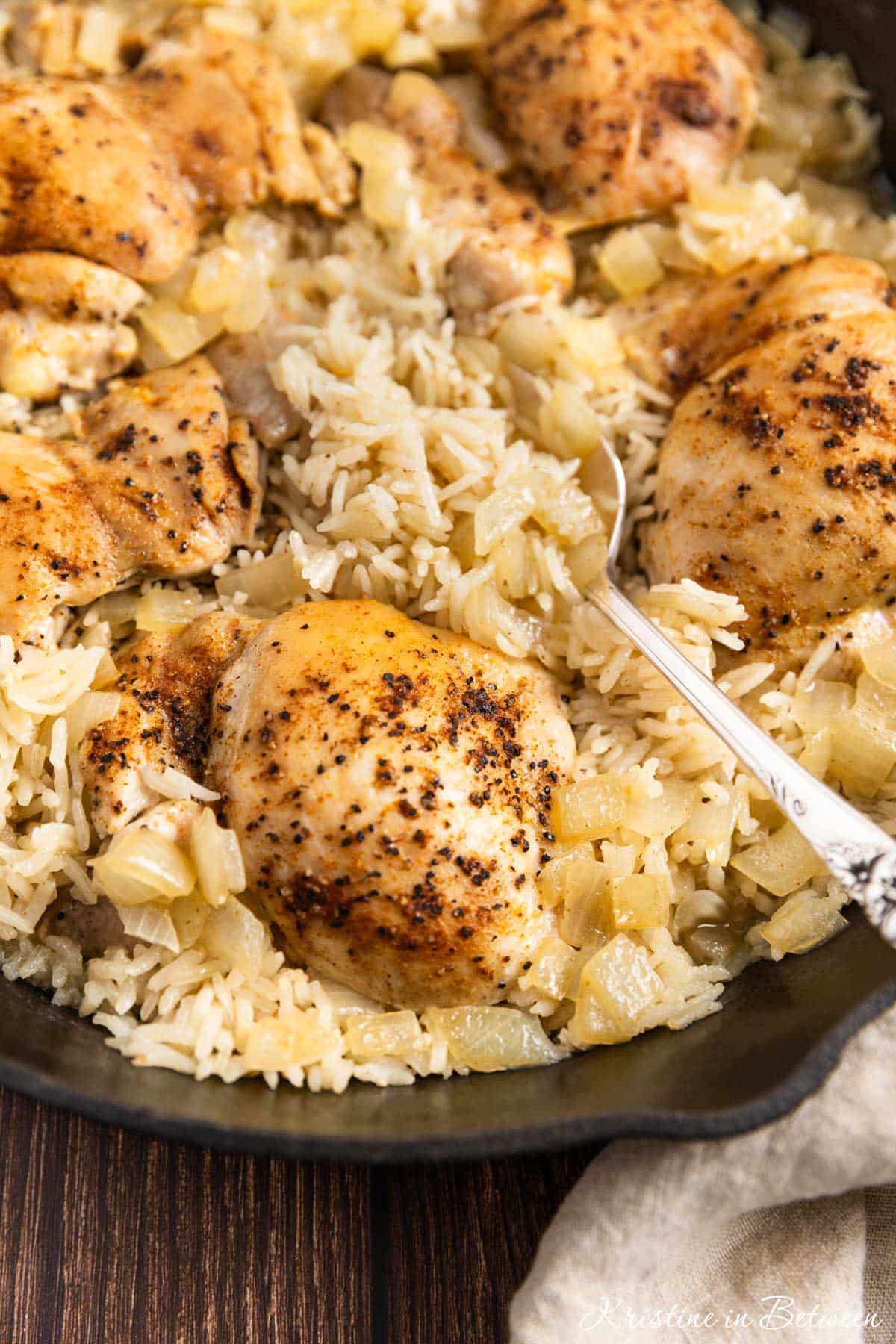Chicken thighs and rice in a cast iron pan with an antique spoon.