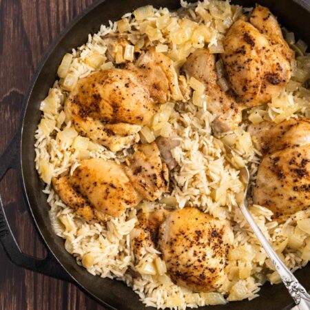 Chicken thighs and rice in a cast iron pan with an antique spoon.