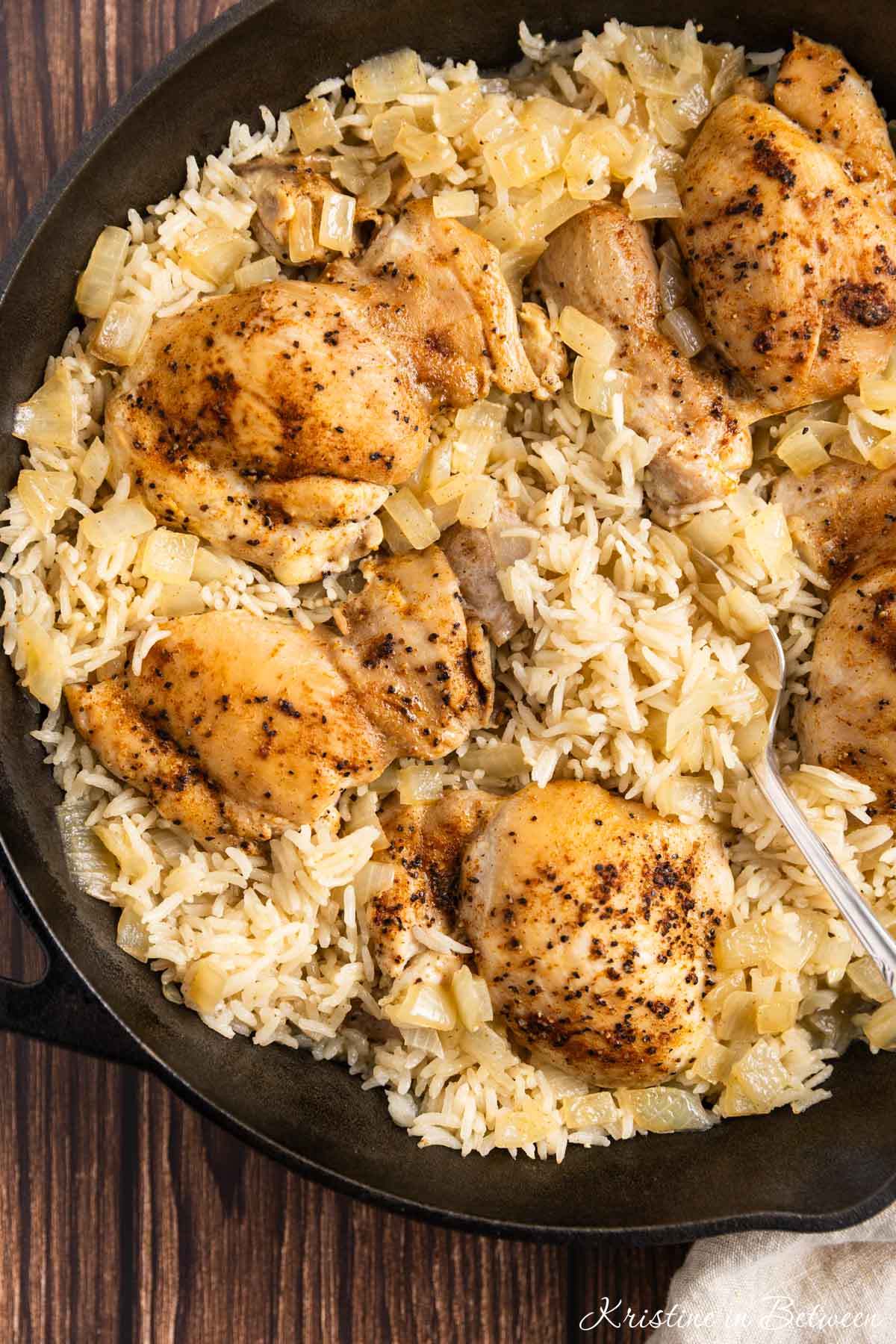 Chicken thighs and rice in a cast iron pan with an antique spoon.